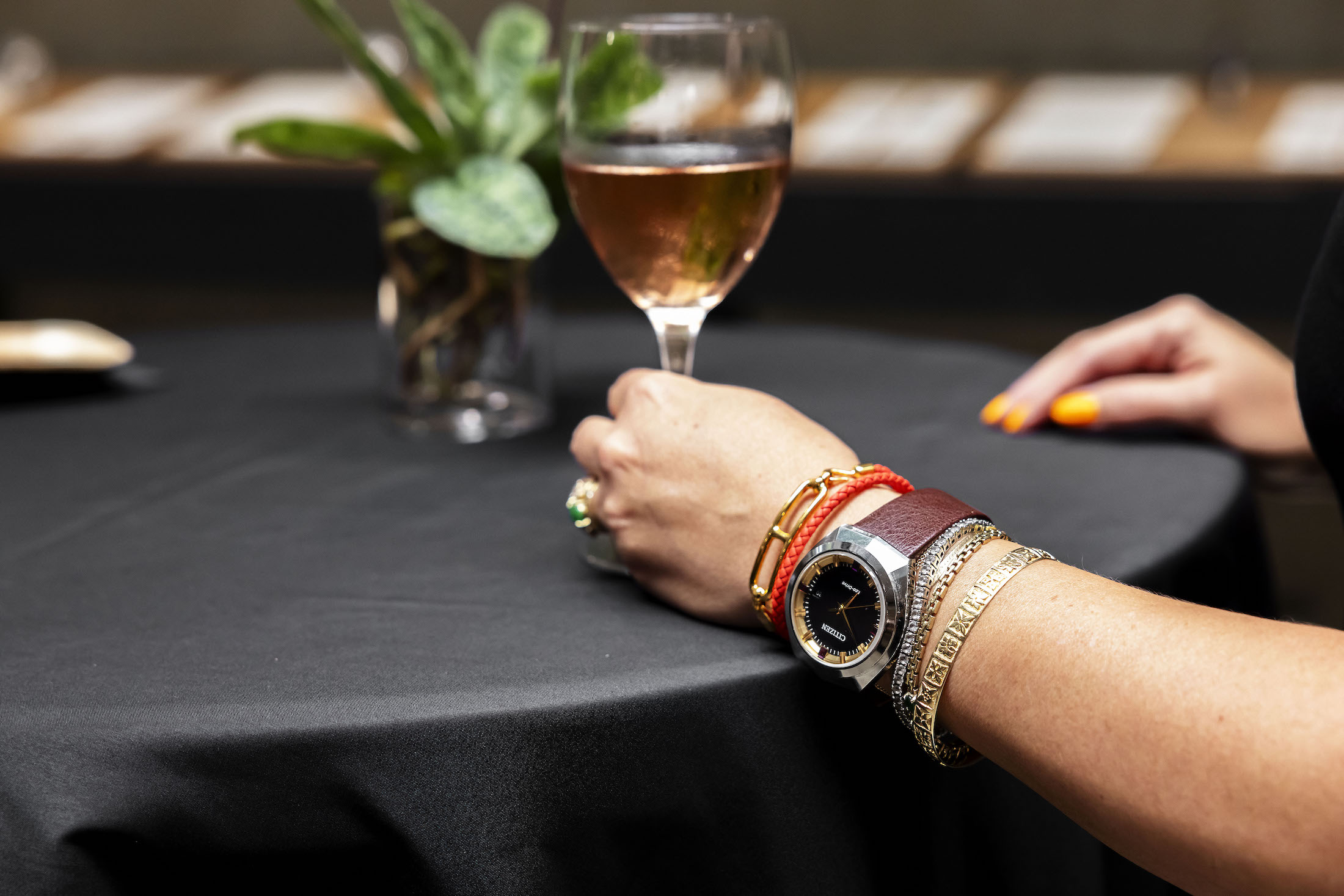 A woman's wrist with a citizen watch, bracelets, and a glass of rose on a table