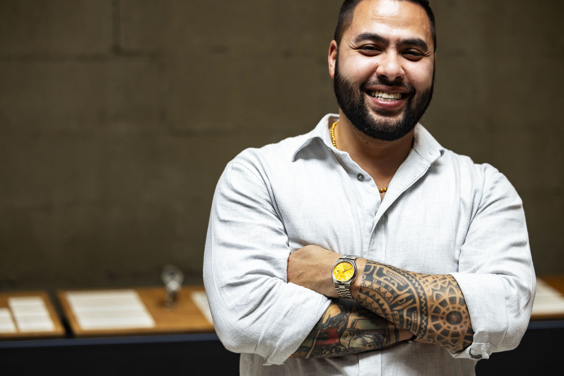 A smiling man with tattoos, showing off a yellow watch