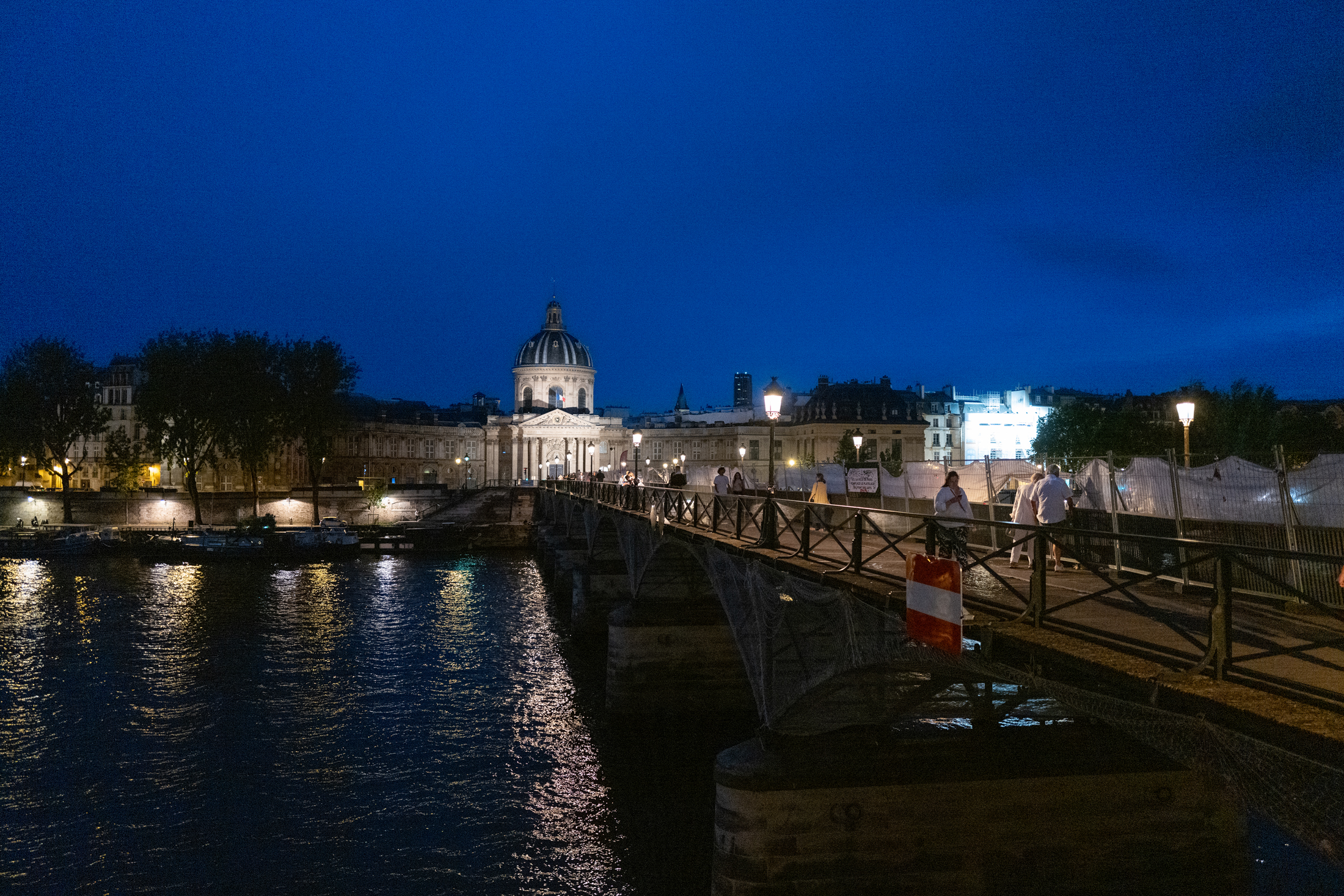 A bridge stretches across a river leading toward an illuminated building in an urban area of Paris at night time