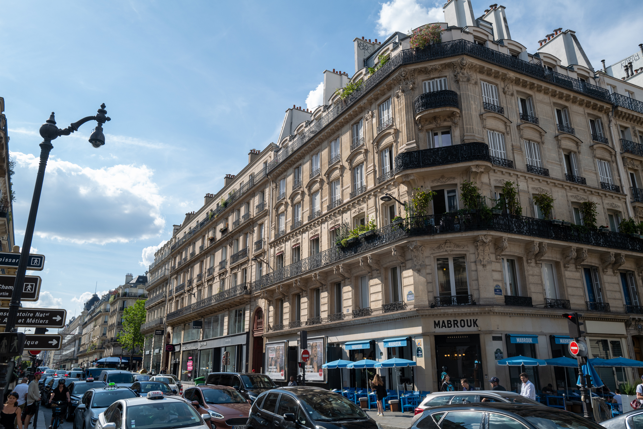 Traffic outside a busy Paris street corner. The front entrance of the building reads "MABROUK"