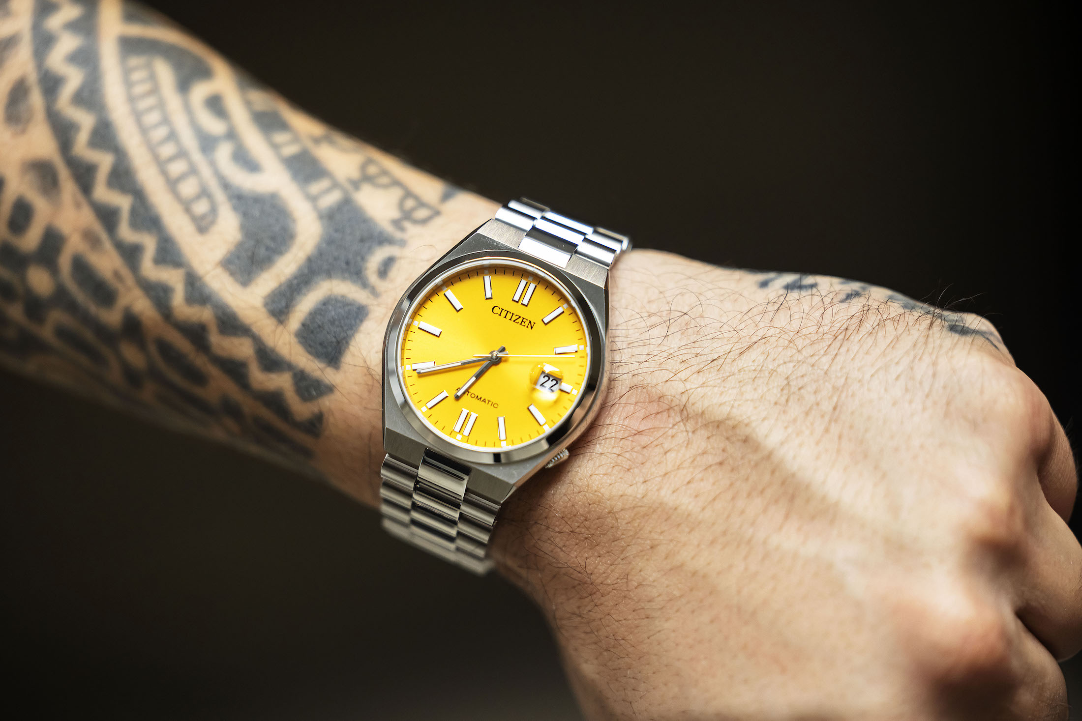 A yellow watch on a tattoo'd wrist